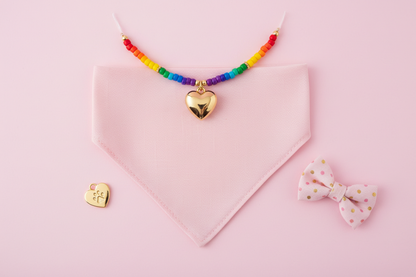 Flat lay of pink dog bandana and rainbow beaded necklace accessories set